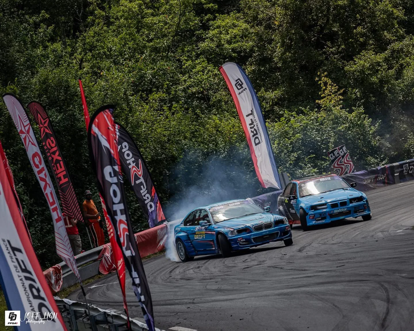 Deux voitures de drift en tandem lors d'une compétition avec signalétique autour de la piste