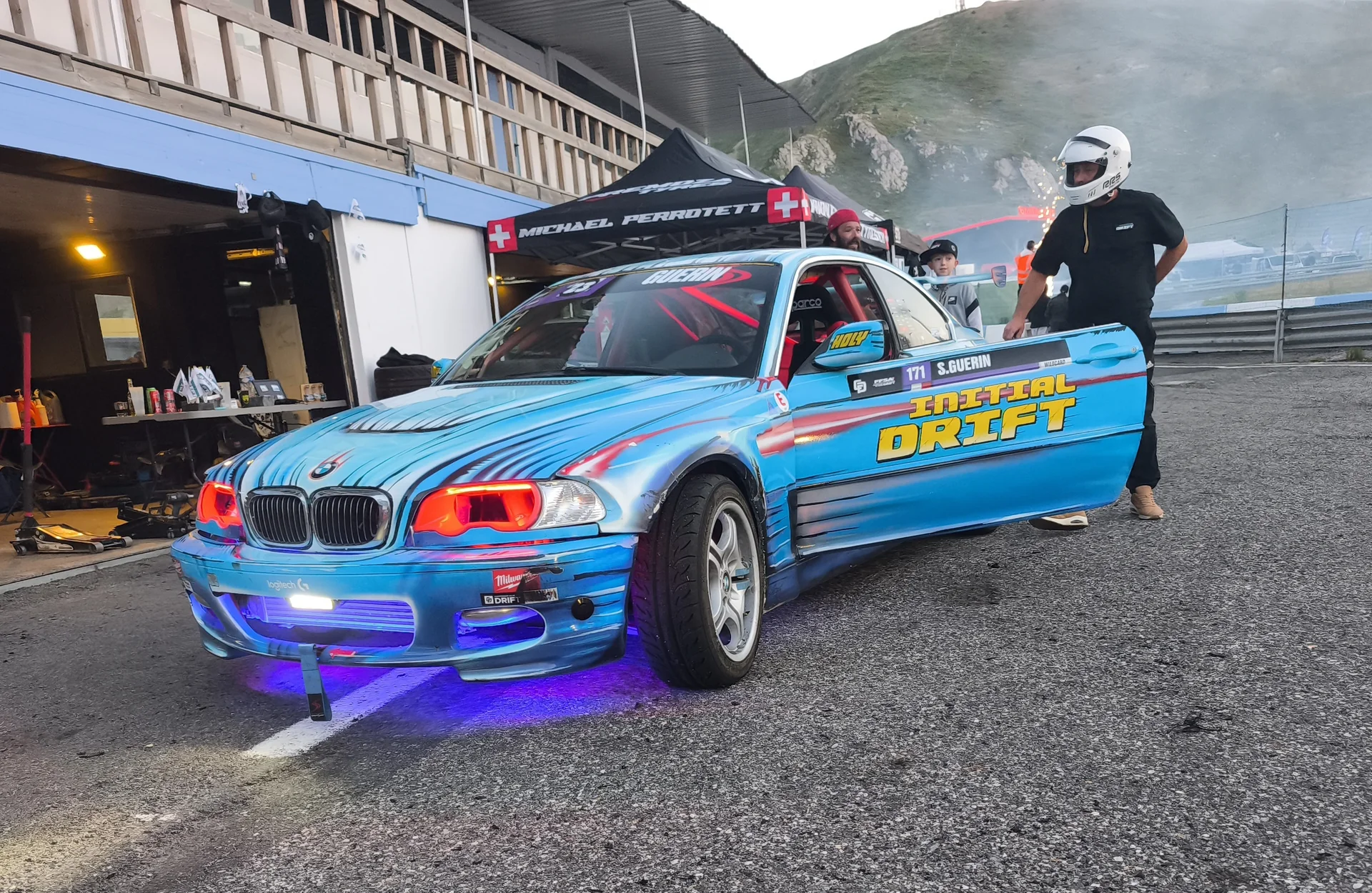 BMW Initial DRIFT dans le paddock, portière ouverte avec membres de l'équipe